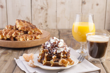 Sweet Belgian waffles for breakfast, decorated with white cream and chocolate sauce. Glass with coffee black and orange juice,fruit bananas and grapfruit. Free space for text or advertising
