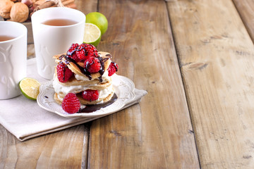 Sweet home punkcakes with white cream and fresh red raspberry berries. Two glasses of tea for breakfast. on a wooden background. free space for text or advertising
