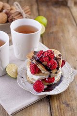 Sweet home punkcakes with white cream and fresh red raspberry berries. Two glasses of tea for breakfast. on a wooden background. free space for text or advertising