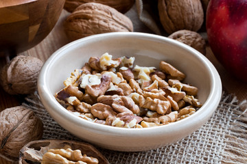 Shelled walnuts in a bowl, with whole walnuts in the background