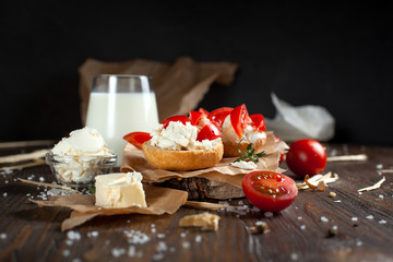 toast with feta cheese on baking paper, a glass of milk, cherry tomatoes and butter on a dark wooden table