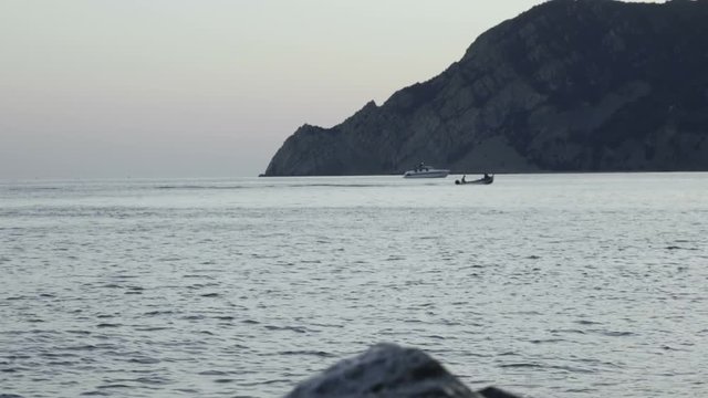 Boat crossing the sea below a cliff, sunset in background.