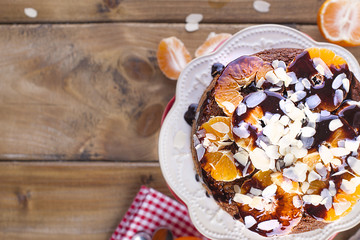 Homemade cake with tangerines and almonds, with chocolate. On a white plate, for breakfast. Wooden background, space for writing text or advertising