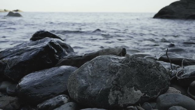 Group of shiny rocks in water, waves crashing on them.