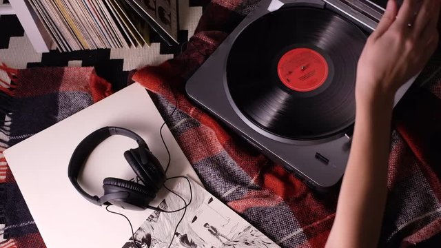 turn-of-2Girl's hand stops turntable vinyl record player with vinyl records, headphones and plaid on the backgrou