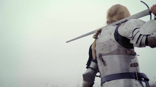 Joan of Arc in knightly armor with a huge sword on her shoulder