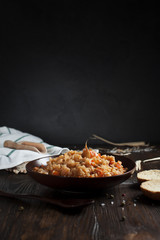 pilau in a brown ceramic dish, a kitchen towel, cherry tomatoes and a basket with spikelets of wheat, bread and a wooden spoon on a dark wooden table
