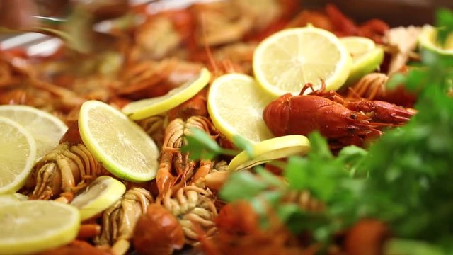 Closeup view of boiled red tasty crayfish on tray on table at restaurant. People take some onto their plates.