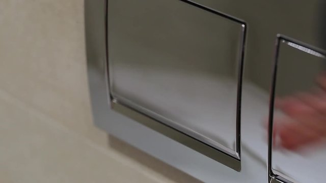 Woman pushing one button of two on wall at bathroom to flush toilet.