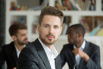 Young serious businessman looking at camera on corporate meeting with partners, professional...