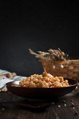 Fototapeta na wymiar pilau in a brown ceramic dish, a kitchen towel, cherry tomatoes and a basket with spikelets of wheat, bread and a wooden spoon on a dark wooden table