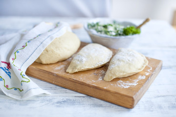 Preparation of homemade pies with fresh herbs and cheese. Dough. A rolling pin and a towel with a pattern. Free space for text or advertising