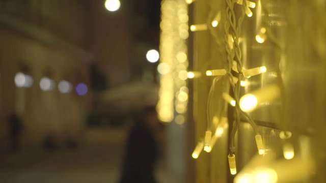 Close up of some christmas lights, yellow-colored, against a wall, street life in background, out of focus.