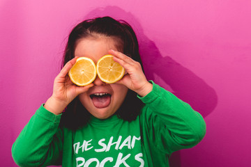 Portrait of a young girl holding two sliced lemons in her eyes and making a silly face