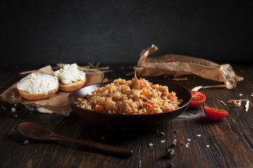 pilaf in a brown ceramic plate, cherry tomatoes, toast with feta cheese and a wooden spoon on a dark wooden table