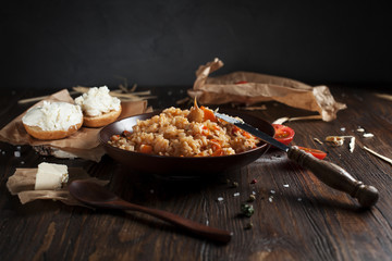 pilaf in a brown ceramic plate, cherry tomatoes, toast with feta cheese and a wooden spoon on a dark wooden table