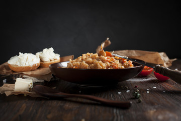 pilaf in a brown ceramic plate, cherry tomatoes, toast with feta cheese and a wooden spoon on a dark wooden table