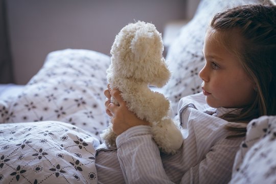 Naklejki Girl holding teddy bear on bed