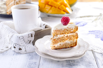 Portion of cake on a small white plate, with a cream for breakfast. A mango fruit. White background, cup of coffee and free space for text or advertising.