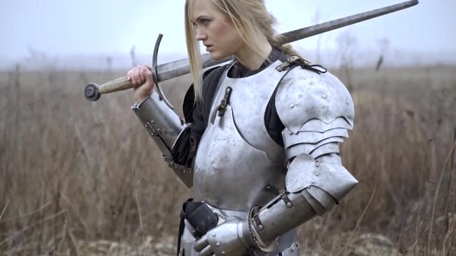 A woman in armor stands in the field and looks around