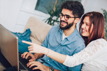 Obraz premium Happy young couple sitting on sofa at home with laptop