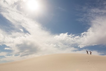 Couple with sandboard walking in sand dune