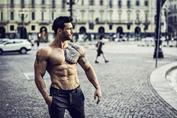 Handsome muscular man with tattoo posing in European city centre. 