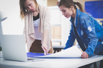 Fototapeta premium Two young woman standing near desk with instruments, plan and laptop.