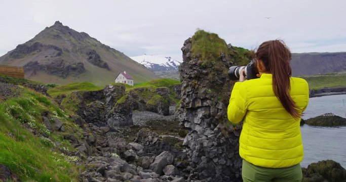 Tourist on travel taking photo with DSLR Camera on Iceland of dramatic nature landscape. Happy woman sightseeing taking pictures using smartphone visiting Arnarstapi, Snaefellsnes, West Iceland.