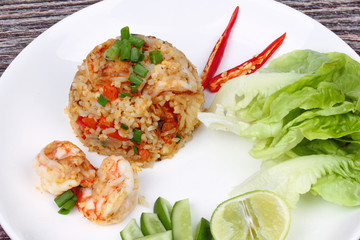 Fried rice with shrimp topped sliced red hot chili pepper,sliced cucumber ,halved green lemon and garlic on white plate.