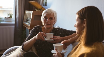 Senior woman and daughter sitting on sofa having a cup of coffee