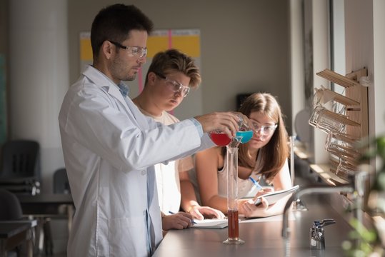 Teacher assisting students in chemical experiment