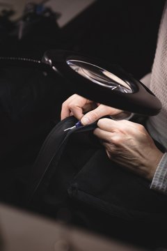Tailor looking through magnifying glass while stitching a