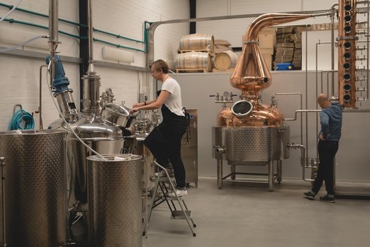 Female worker checking machine of distillery - Powered by Adobe