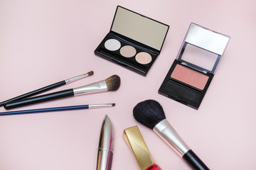 Ladies fashion accessories. Eye shadow, blush, lipstick, makeup brushes, mascara on a pink background.