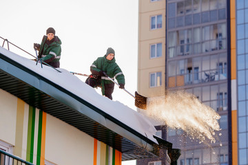 Snow cleaning. Team of male workers clean roof of building from snow with shovels in securing belts...