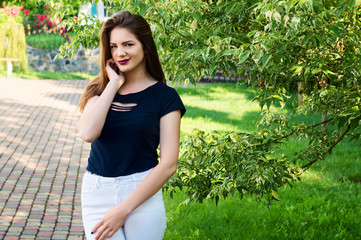 Fototapeta premium Beautiful model in a black T-shirt and white pants in a park in the middle of green trees.