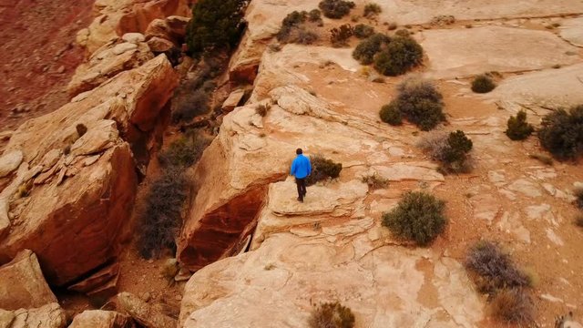 Aerial shot of a man hiking along the edge of amazing rock formations in Utah.