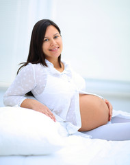 Beautiful pregnant woman sitting at sofa and keeping hand on belly.