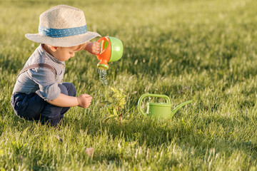Toddler child outdoors. One year old baby boy wearing straw hat using watering can © haveseen
