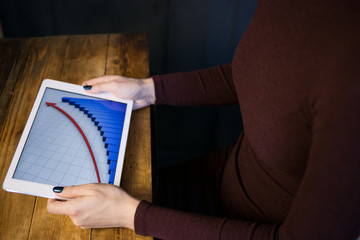 The girl working with a tablet computer. The graph rises. Table, wooden, background black.