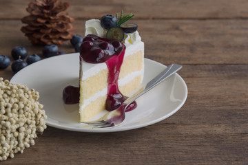 Blueberry cream cake on white plate on wood table with copy space. Vanilla sponge cake decorated with dairy whipped cream and blueberry sauce so soft sweet and delicious. Homemade bakery concept.