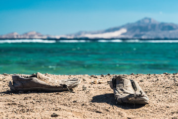 Fototapeta na wymiar Pair of old shabby shoes on the sandy beach. Old shabby shoes on the sand.