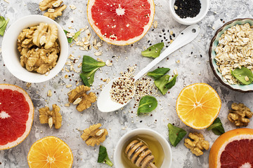 Ingredients of healthy breakfast food: oat flakes, kinoa, walnuts, floral honey, greens, oranges, bloody grapefruits on a light marble background. Top View.