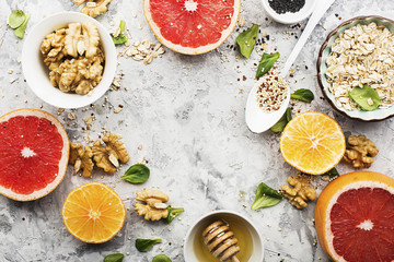 Ingredients of healthy breakfast food: oat flakes, kinoa, walnuts, floral honey, greens, oranges, bloody grapefruits on a light marble background. Top View.