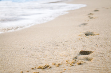 Footprints in the sand at sunset. Beautiful sandy tropical beach with sea waves. Footsteps on the shore.
