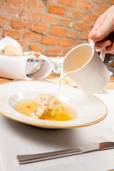 Broth with dumplings and an egg yolk being poured from a jug