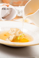Broth with dumplings and an egg yolk being poured from a jug