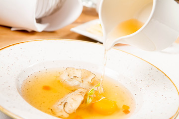 Broth with dumplings and an egg yolk being poured from a jug