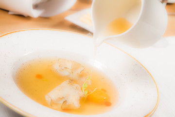 Broth with dumplings and an egg yolk being poured from a jug